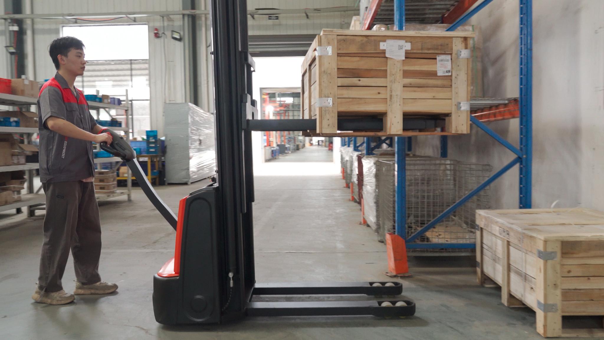 Operator using EP Equipment ESA121-D electric walkie stacker to lift and move wooden crates safely in narrow warehouse aisles.