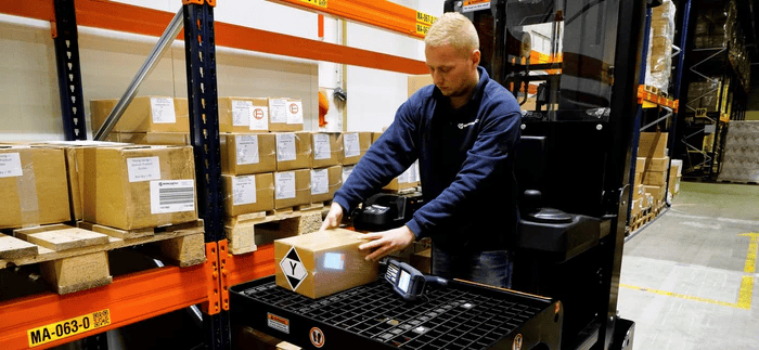 Operator using EP Equipment JX1 electric order picker to handle packages on warehouse shelves.