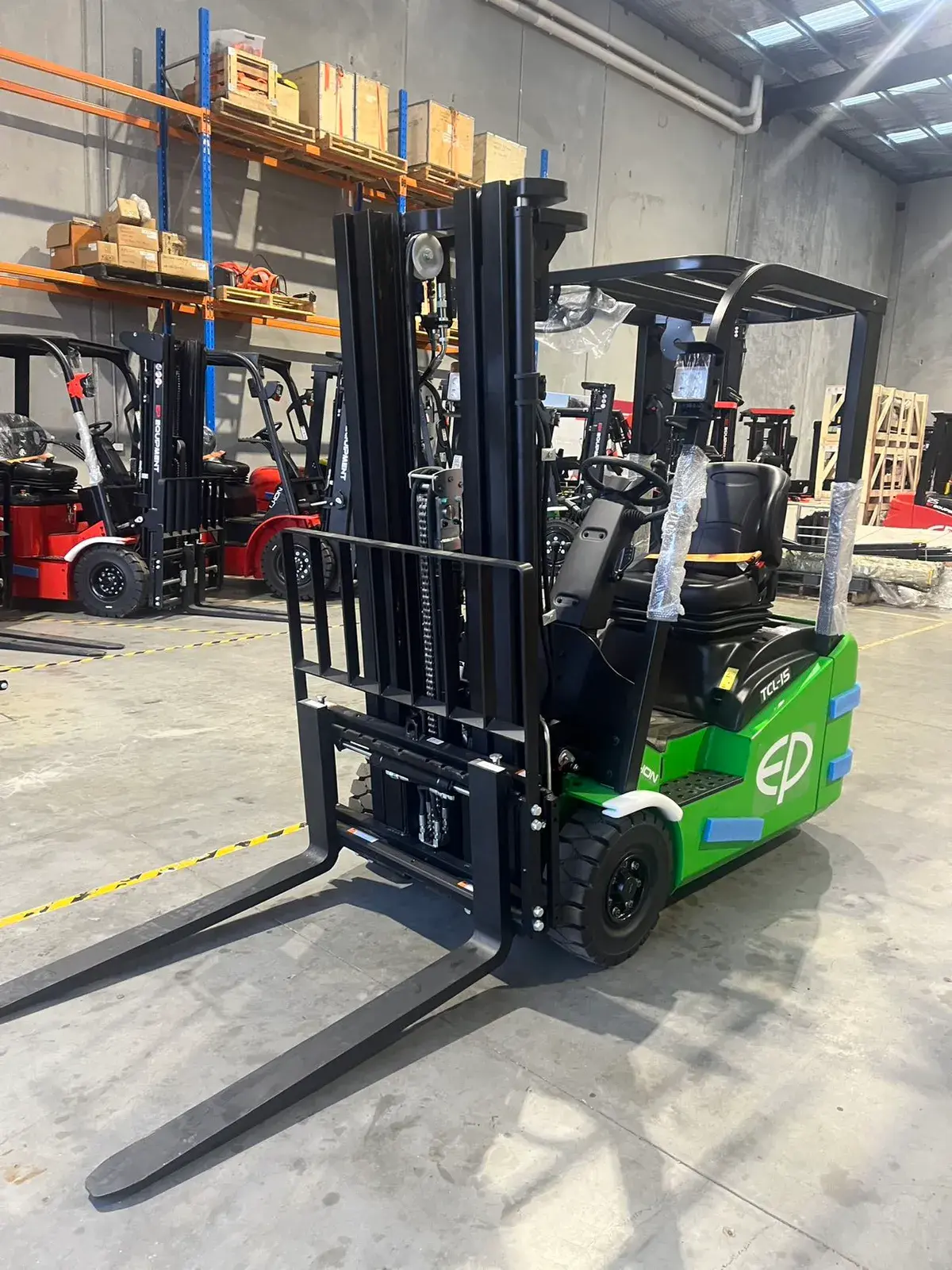 Front-left view of an EP Equipment TCL152 1.5T three-wheel electric forklift in a warehouse, showing the triplex mast and fork carriage