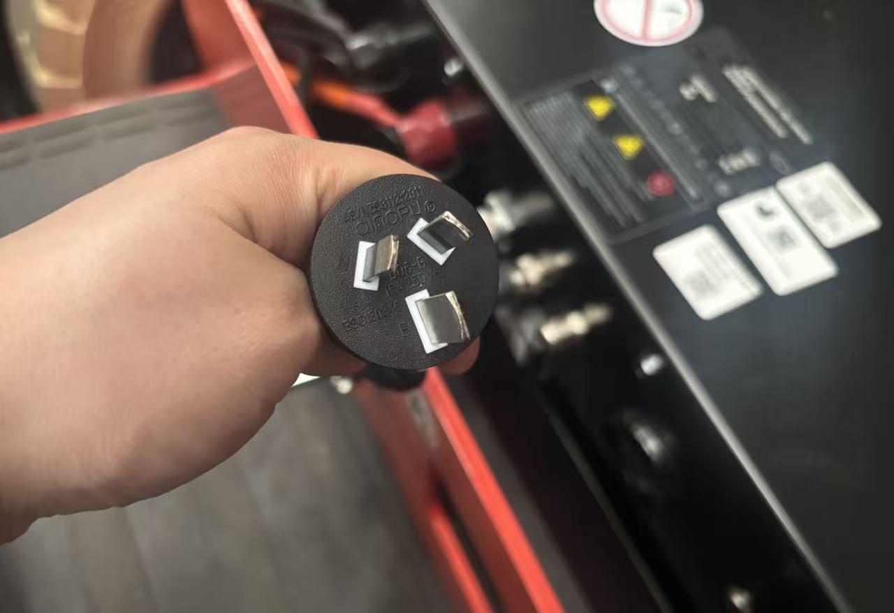 Operator holding integrated on-board charger plug for electric forklift, enabling simple charging via standard outlet