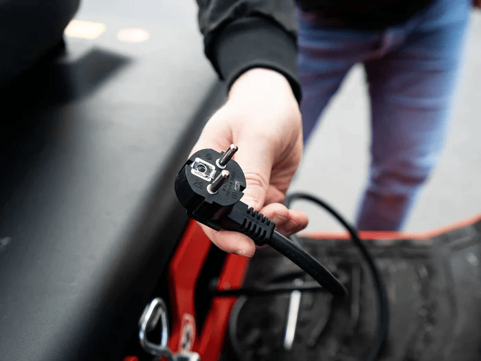 Operator holding integrated on-board charger plug for electric forklift, enabling simple charging via standard outlet