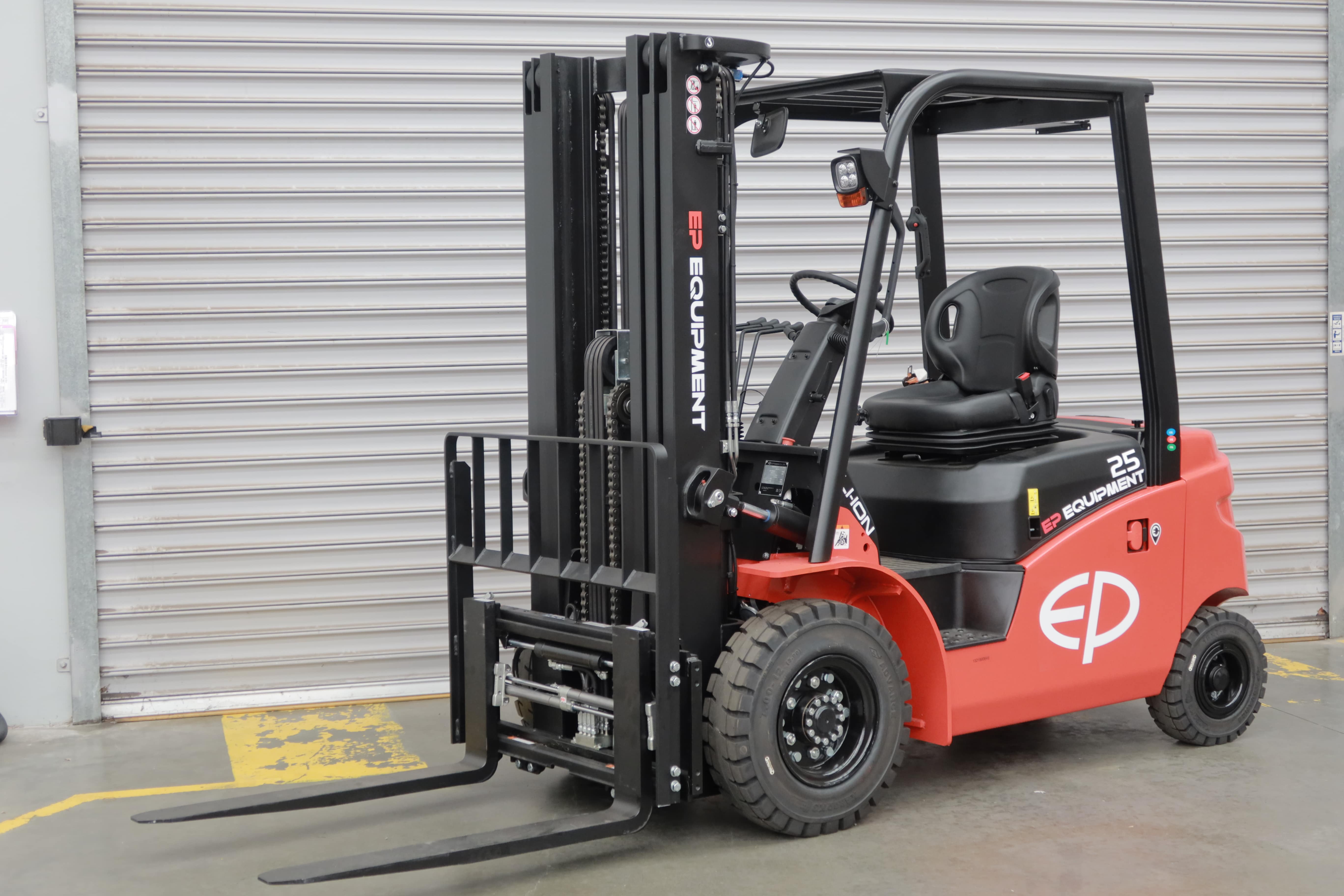 EFL253 four-wheel lithium counterbalance forklift by EP Equipment parked in front of warehouse roller door