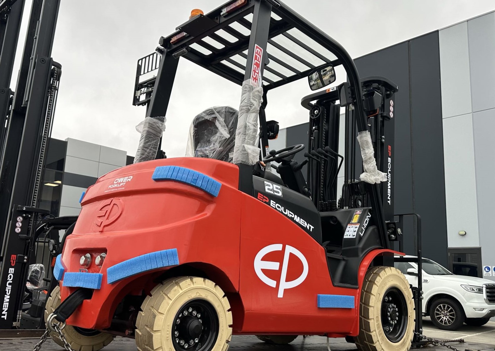 Brand new EFL253 lithium counterbalance forklift by EP Equipment, wrapped for delivery and parked outside warehouse facility