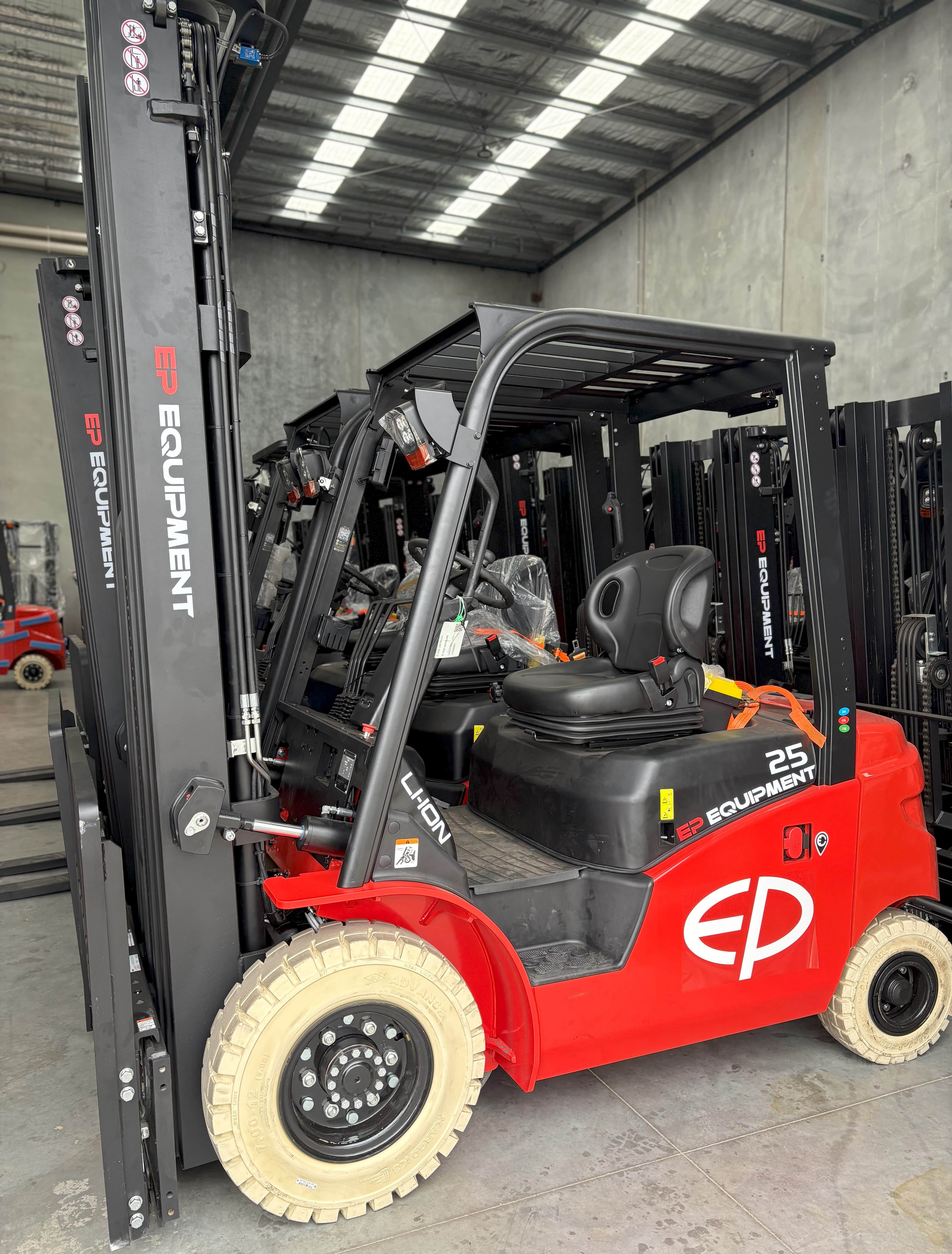 EFL253 four-wheel lithium counterbalance forklift by EP Equipment stored in warehouse with other forklifts