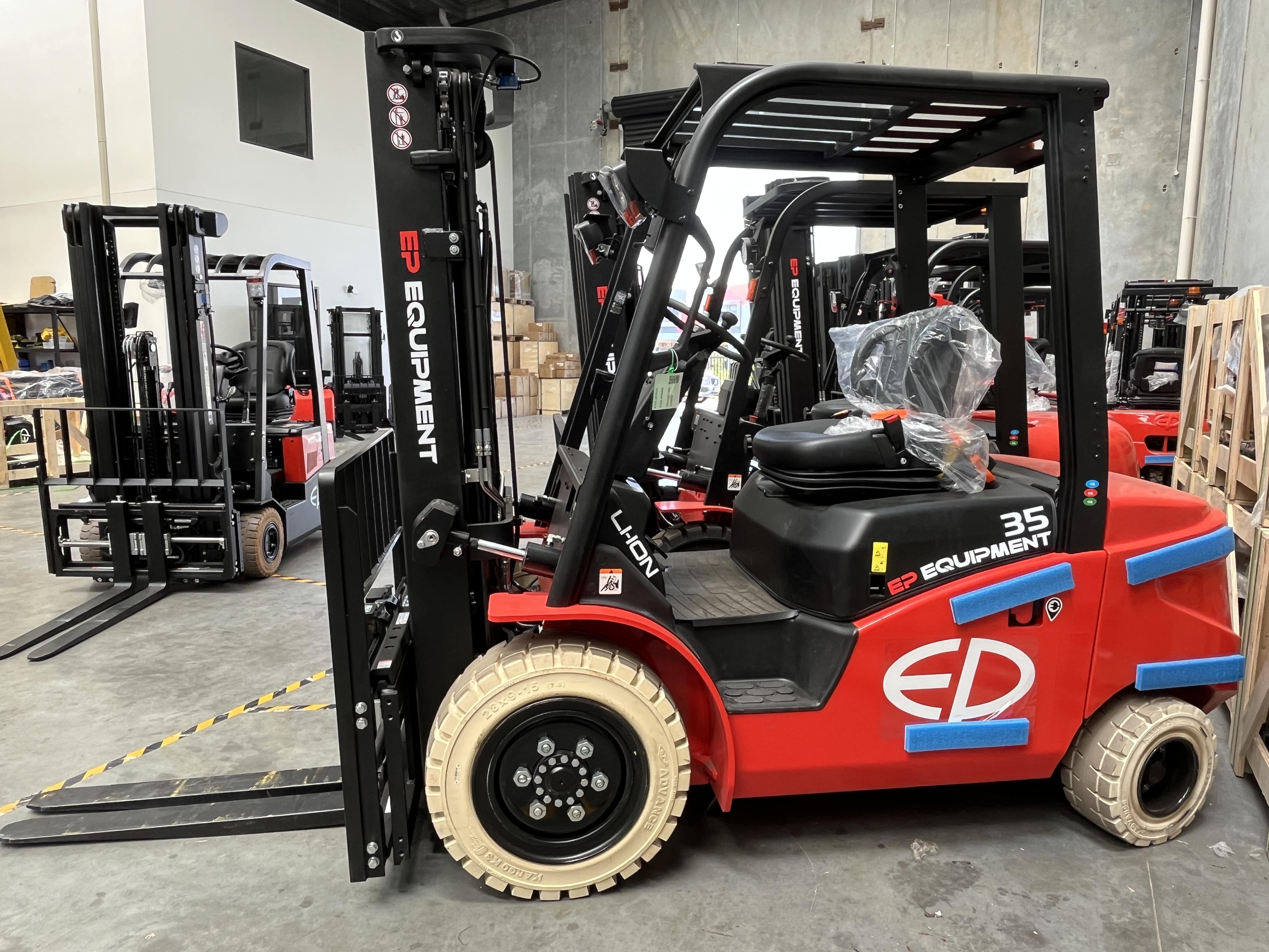 Side view of EFL353 four-wheel lithium counterbalance forklift by EP Equipment stored in warehouse with other forklifts