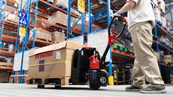 Operator using EP Equipment F4 electric pallet truck to move heavy loads in warehouse aisles.